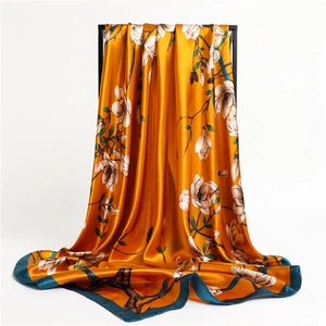Détail d'un foulard en soie dorée avec motif floral blanc et bordure vert foncé