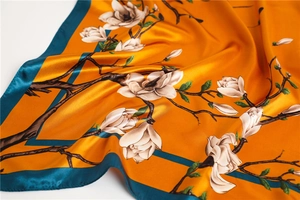 Gros plan détaillé du foulard en soie orange avec des magnolias et fini satiné