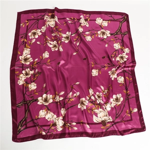 Détail d'un foulard carré en soie rose foncé avec motifs de magnolia et texture satinée