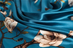 Détail d'un foulard carré en soie avec de magnolias blancs sur un tissu en satin bleu sarcelle