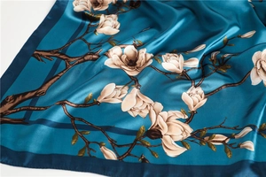 Détail d'un foulard en satin bleu canard avec imprimé magnolia et texture soyeuse fine