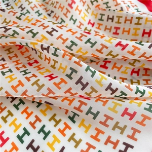 Detailaufnahme eines Seiden-Vierecktuchs mit bunten H-Buchstaben und glatter Textur