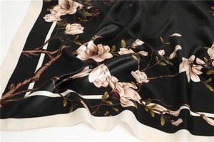 Détail du foulard en soie noir avec motif de magnolia et bordure crème contrastée
