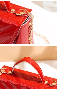 Detail of red patent leather crossbody bag featuring chevron quilting and gold chain