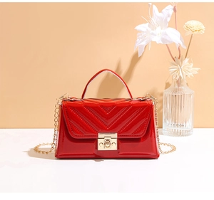 Detail of red patent leather handbag with V-shaped quilting and gold square lock