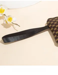 Detail of a brown clutch bag with golden clover patterns and black litchi grain wristlet