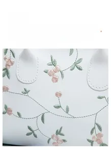 Close-up of elegant floral embroidery with green leaves on white leather handbag detail
