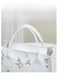 Close-up of elegant floral embroidery and comfortable handle on a white tote bag