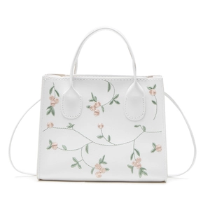 White faux leather handbag featuring elegant floral embroidery and adjustable shoulder strap