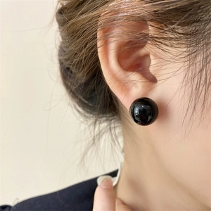 Close-up of a glossy black round stud earring worn on the earlobe with elegant look