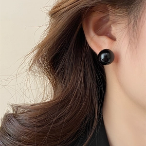 Close-up of minimalist black pearl stud earrings with high-gloss finish on model's ear