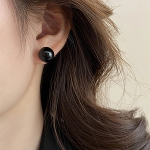 Close-up of minimalist black pearl stud earrings with a glossy mirror finish on model