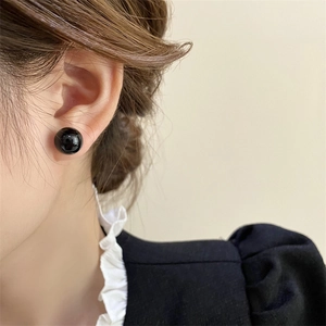 Close-up of a glossy black pearl stud earring worn on a model ear with soft lighting