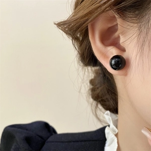 Close-up of 8mm round black pearl stud earring with a high-gloss finish worn on the ear