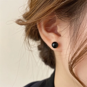 Close-up of elegant black pearl stud earring worn on ear with polished finish