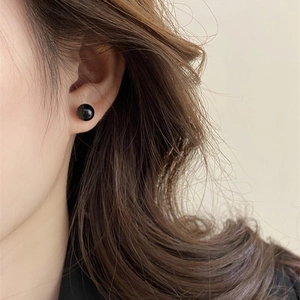 Close-up of a glossy black pearl stud earring worn on a model for a chic look