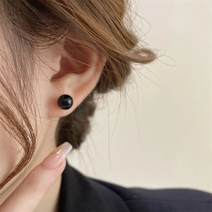 Close-up of minimalist round black pearl stud earring with a glossy mirror-like finish