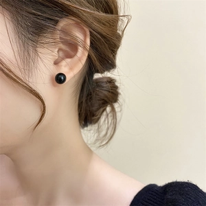 Close-up of minimalist black pearl stud earring with glossy finish on a female model