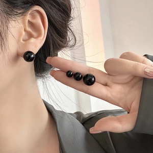 Detail view of black pearl stud earrings in four sizes showing high-gloss reflection