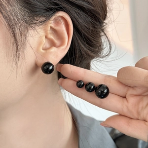 Detail view of various sizes of glossy black pearl stud earrings shown on fingertips
