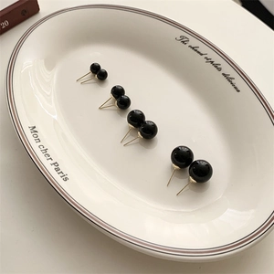 Detail showing four sizes of black pearl stud earrings with gold pins in a ceramic dish