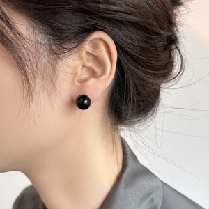 Close-up of elegant black spherical stud earrings with a glossy mirror finish on a model