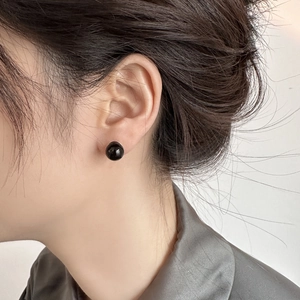 Close-up of polished 10mm black pearl stud earrings worn by a model in natural light