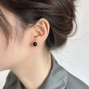 Close-up of 8mm black round pearl stud earrings on model's ear with glossy finish