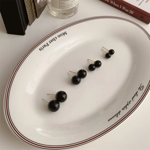 Detailed view of black round stud earrings in four sizes on a vintage ceramic tray
