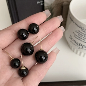 Elegant black pearl stud earrings in various sizes with gold posts held by hand