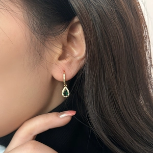 Detailed shot of emerald pear-cut zircon earrings with gold plating and pavé setting