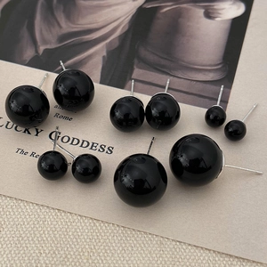 Macro detail of glossy black pearl stud earrings in five sizes on vintage artistic display card