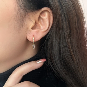 Detail of gold zircon earrings with rectangular crystal pendant on a model's ear