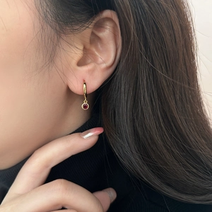 Close-up of a gold huggie earring with a round red gemstone pendant on a model's ear