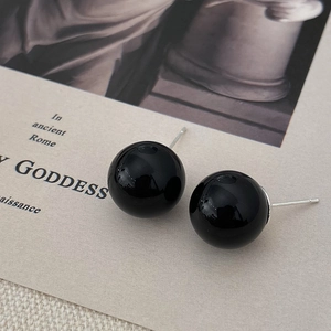 Macro detail of elegant black pearl stud earrings with silver pins on a vintage card