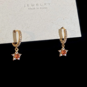 Detail of gold star earrings with orange gemstones and white cubic zirconia accents