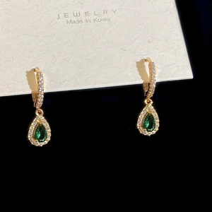 Detailed shot of gold earrings featuring pear-cut emerald gemstones and white zircons