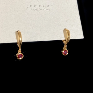 Detail of gold hoop earrings with ruby red pendant displayed on a premium white jewelry card