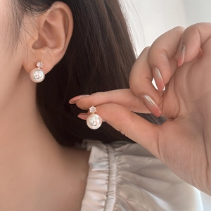 Detailed view of elegant white round pearl earrings with zircon inlay in gold setting