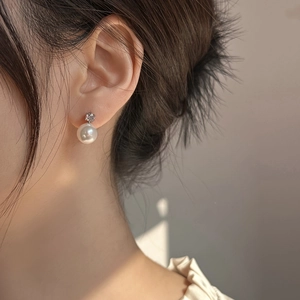 Close-up of a white pearl earring with a sparkling zircon stud on model's ear