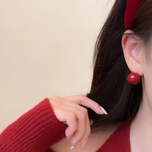 Primer plano de un elegante pendiente de esfera roja con base dorada en la oreja del modelo
