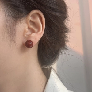 Detalle de un elegante pendiente de bola rojo oscuro que lleva puesto una modelo