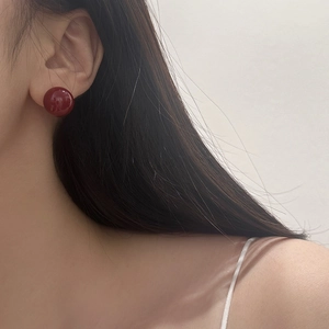 Primer plano de pendientes de bola rojo oscuro pulidos usados por una modelo