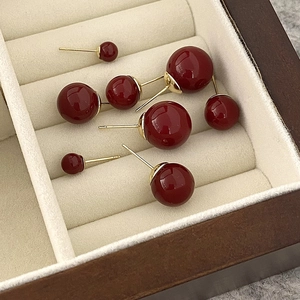 Macro de elegantes pendientes de esfera rojo oscuro en varios tamaños sobre terciopelo