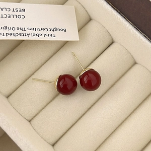 Primer plano de pendientes de perlas rojo oscuro en estuche de terciopelo beige y oro