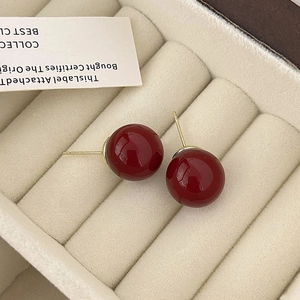 Primer plano de pendientes de bola rojo oscuro pulido en un joyero de rayas color crema