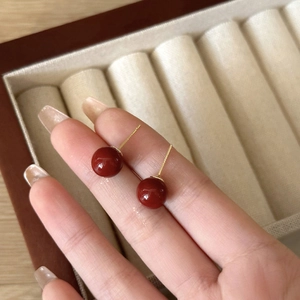 Primer plano de pendientes de perlas rojas con postes dorados mostrando el tamaño real