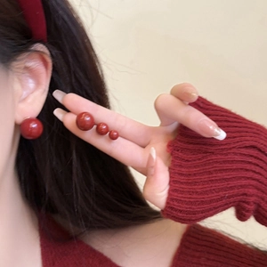 Pendientes de bola roja en varios tamaños mostrados en modelo con tonos festivos