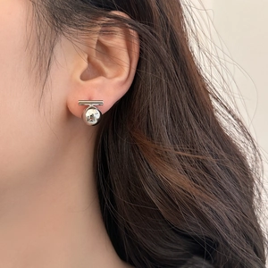 Close-up of a silver bar and ball geometric stud earring on a model ear