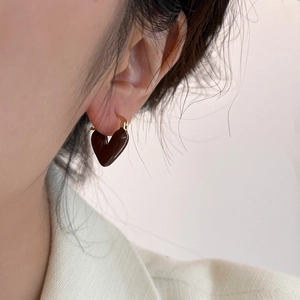 Close-up of a heart-shaped dark brown enamel earring with a gold hoop worn on ear
